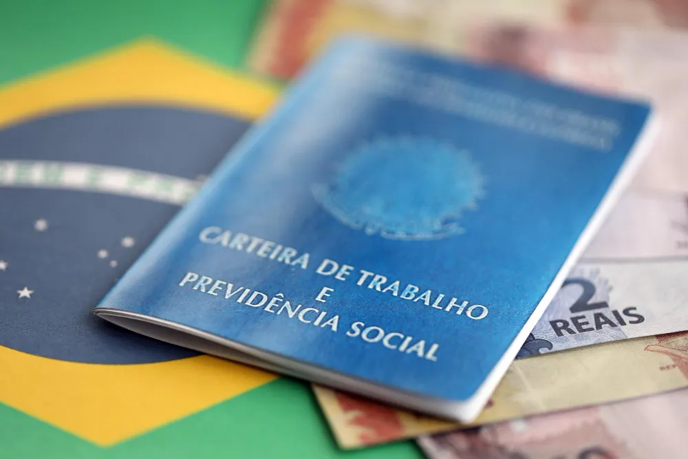 Carteira de Trabalho e Previdência Social sobre bandeira do Brasil e notas de dinheiro, para saber qual o valor do auxílio-acidente.
