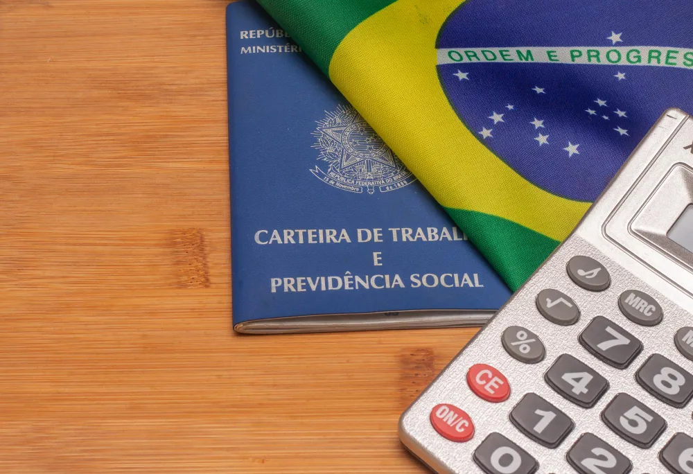 Carteira de Trabalho, bandeira do Brasil e calculadora para saber qual o valor do auxílio-acidente.